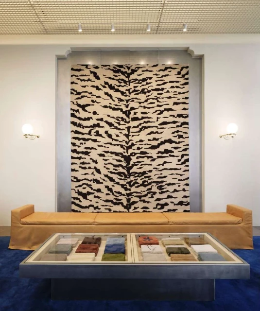 Interior design featuring a tiger-striped rug hanging on the wall, a sofa, and a coffee table with fabric samples in a showroom setting.