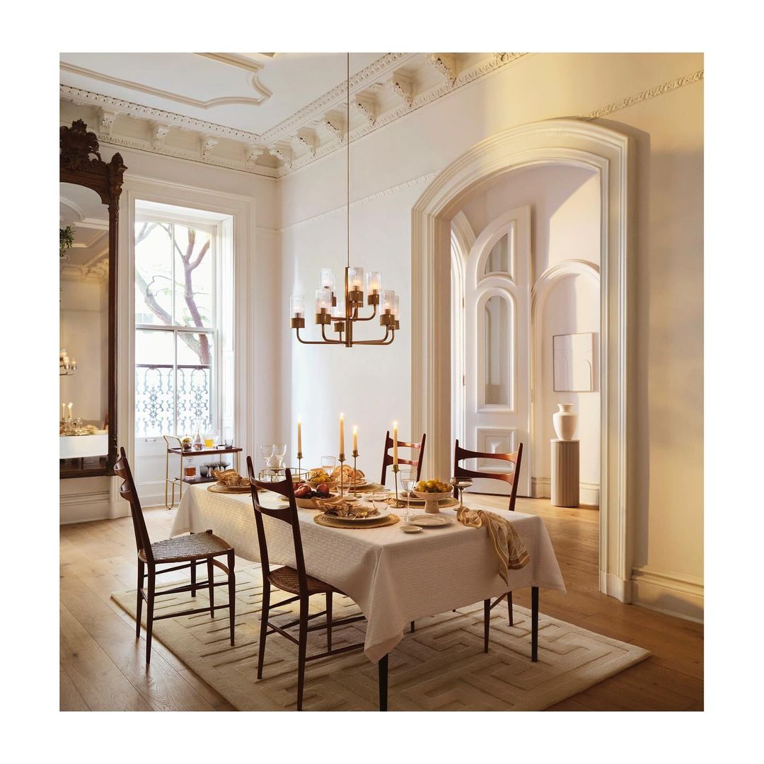 Formal dining room interior: A dining table is set for a meal with a chandelier above, in a light-filled room with architectural details.