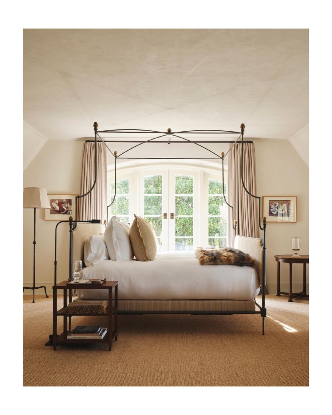 Bedroom interior featuring a four-poster bed, neutral color scheme, natural light from large windows, and classic furniture arrangement.