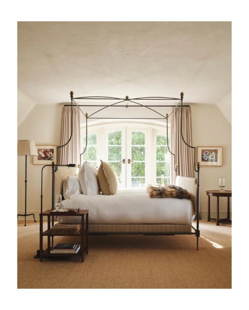 Bedroom interior featuring a four-poster bed, neutral color scheme, natural light from large windows, and classic furniture arrangement.