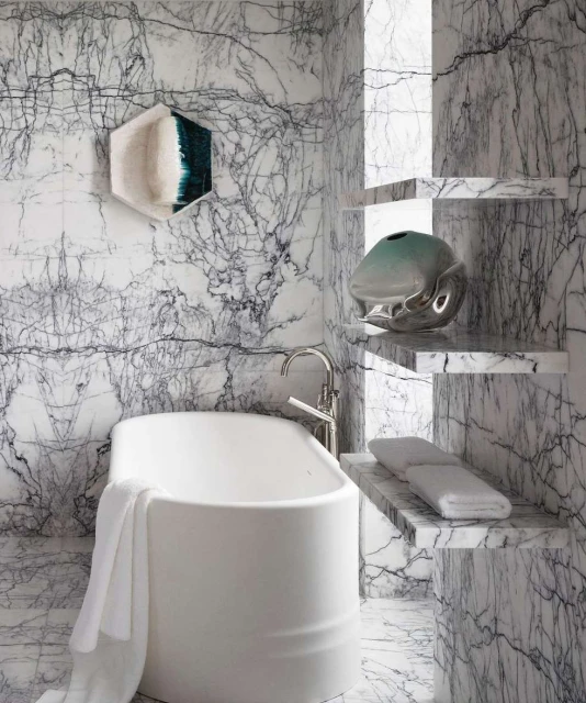 Modern bathroom interior featuring a white bathtub, marble walls and shelves, and decorative vases in a bright, clean setting.