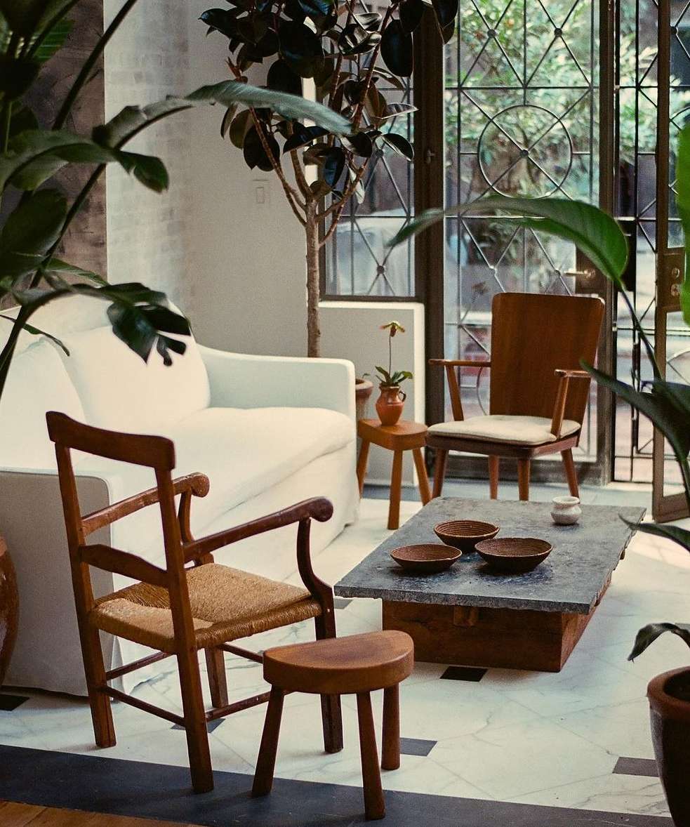 Living room interior with a white sofa, wooden chairs, a stone coffee table, and potted plants creating a natural and inviting space.