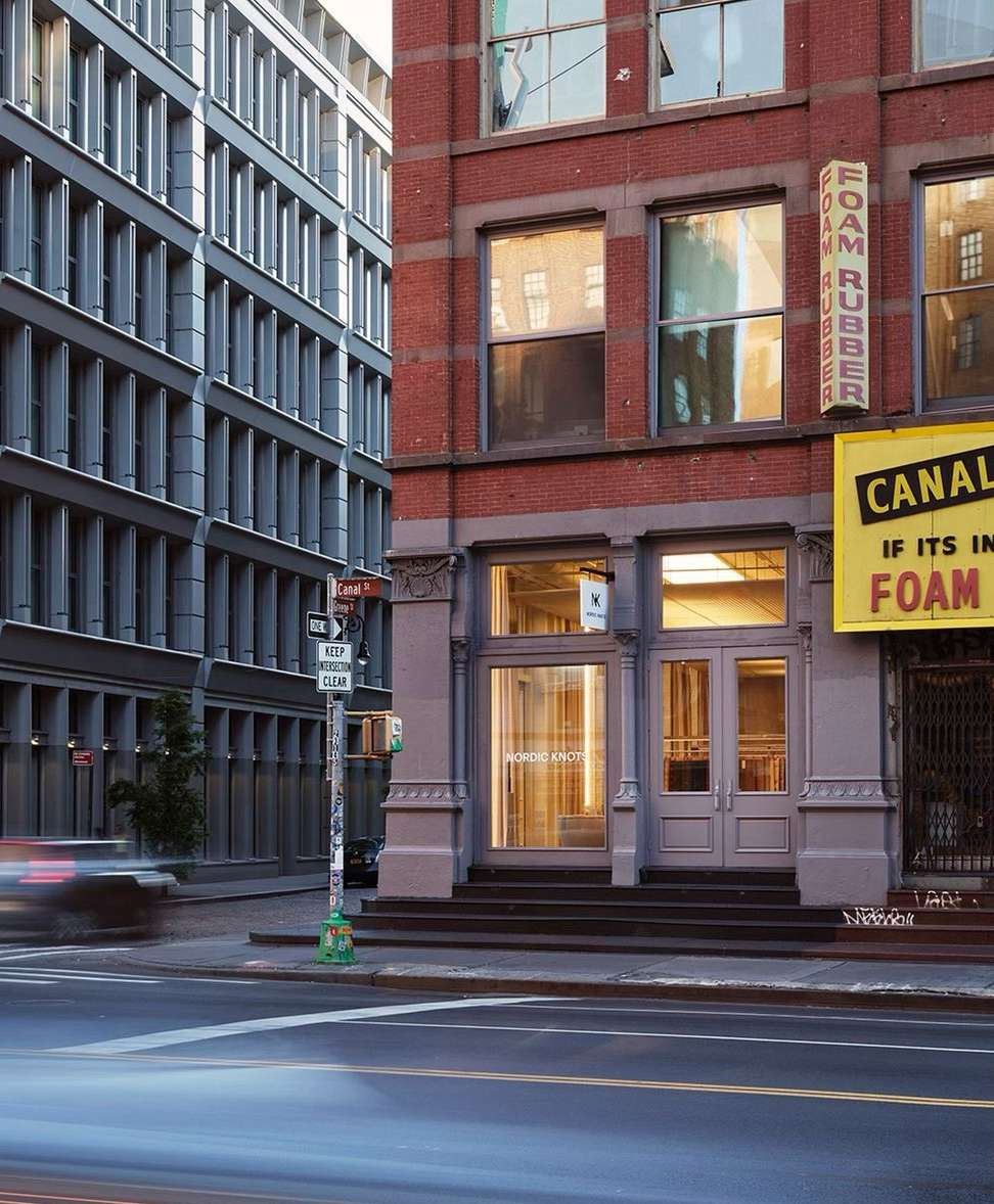 Exterior view of a red-brick building with large windows and signage, next to a modern building on a city street at dusk.