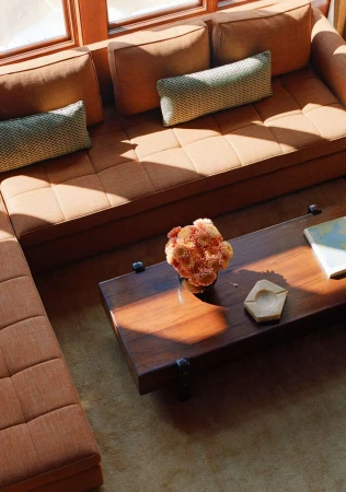 Modern interior featuring a tan sectional sofa, dark wood coffee table with floral arrangement, light-colored rug, and natural light.