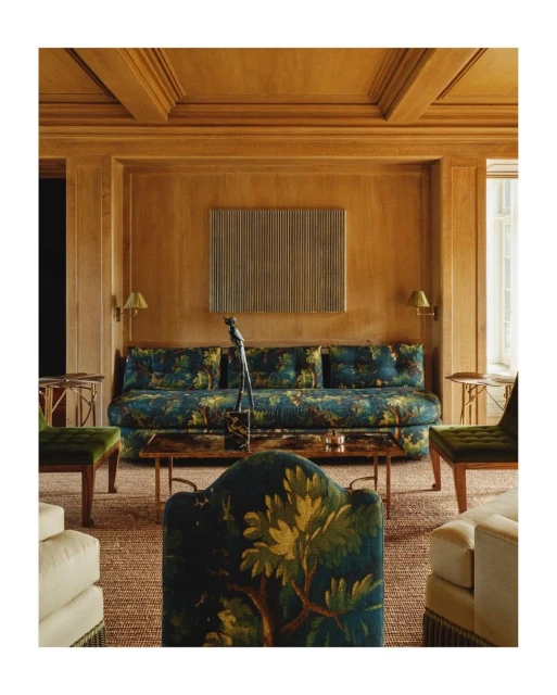 Living room interior showcasing a blue floral patterned sofa, decorative armchairs, brass table, wood paneled walls and ceiling.