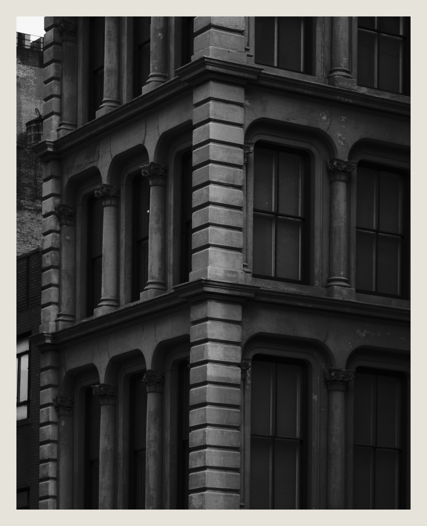 Black and white architectural shot of a building corner with classical features, columns, and windows, showcasing historic urban design.
