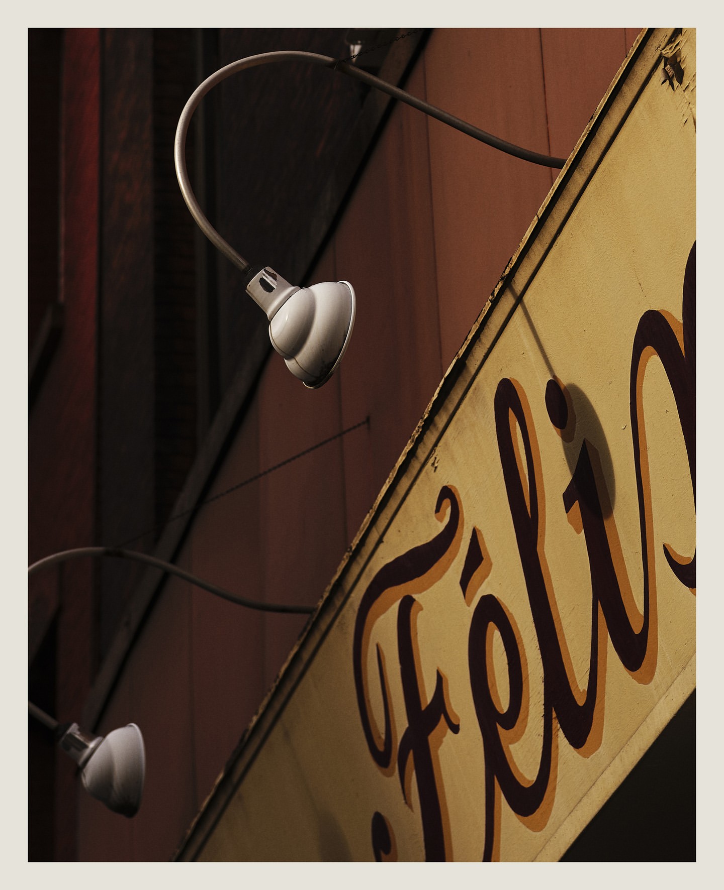 Exterior shot of a building with a light-yellow sign featuring elegant, brown script under two arched lamps on a wood-paneled wall.