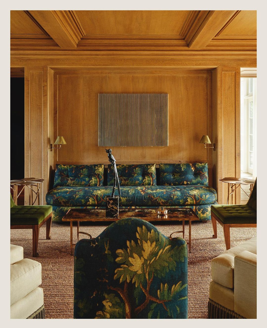 Interior living space showcasing a couch with a botanical print, chairs, a guitar, a sculpture, and warm, neutral color tones.
