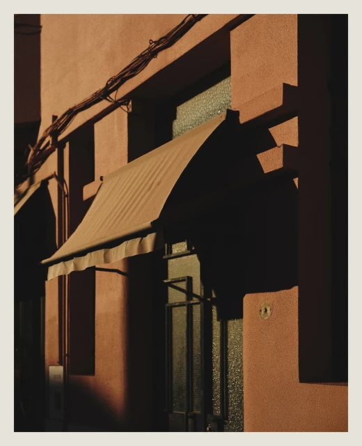 Exterior of a building with a closed awning and a dark entrance, under strong lighting, with pink walls and an urban setting.