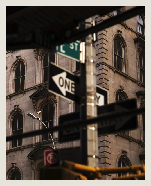 Urban view of a corner building facade with arched windows, street signs, and a traffic light pole in New York City.