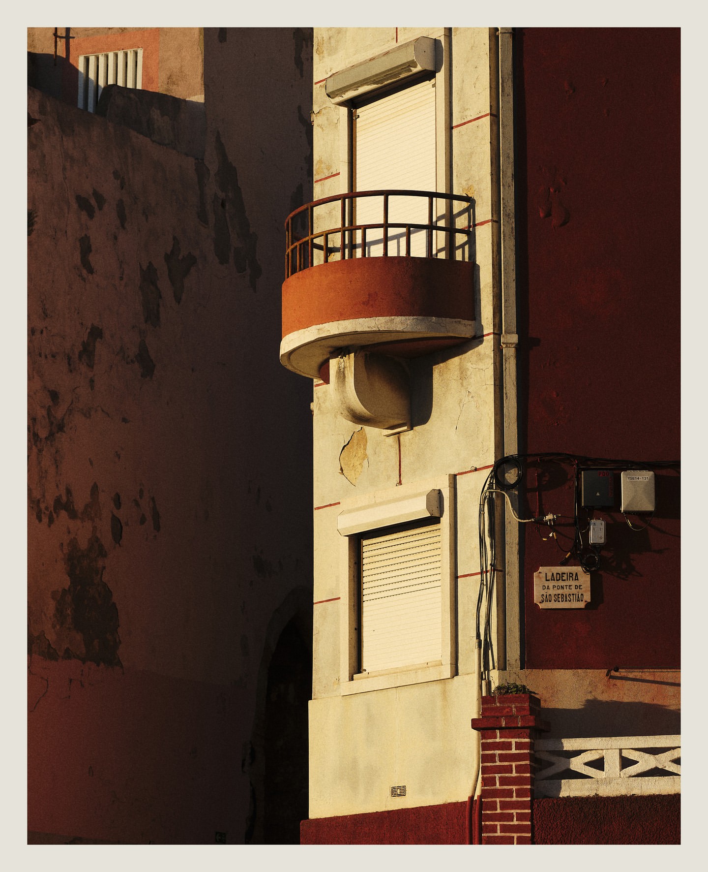 Exterior view of a building facade with a small balcony, featuring a mix of architectural styles and textures in warm, natural light.
