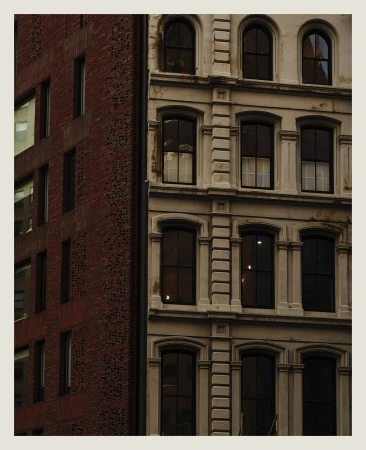 Exterior view of two buildings in an urban environment, one with red brick and the other with a light beige facade, multiple windows.