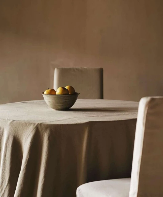 Still life composition with a bowl of lemons on a table with linen, set in an indoor room with soft, diffused lighting.