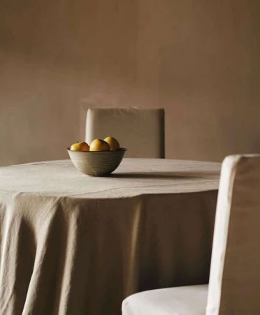 Still life composition with a bowl of lemons on a table with linen, set in an indoor room with soft, diffused lighting.