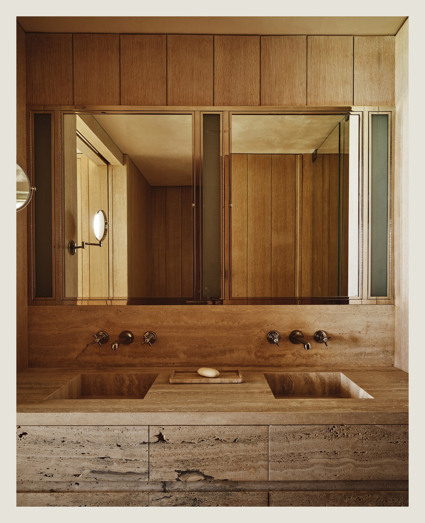 Bathroom interior with a double sink, two mirrors, wooden cabinets, and warm lighting creates a luxurious, functional space.