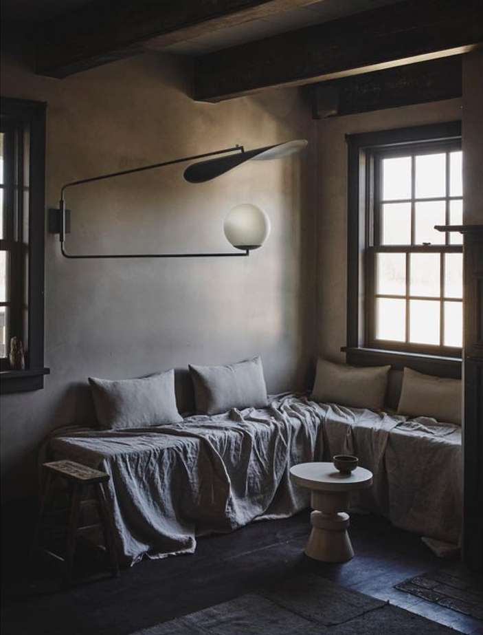 Interior view of living space with a linen-covered daybed, side table, and unique modern lighting fixture with dark wood ceiling beams.