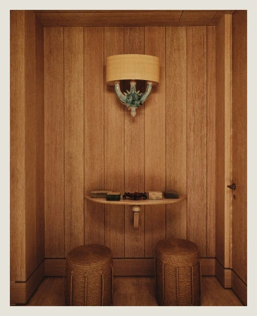 Interior shot of a wood-paneled room with a light fixture, small table holding various small boxes, and two wicker stools.