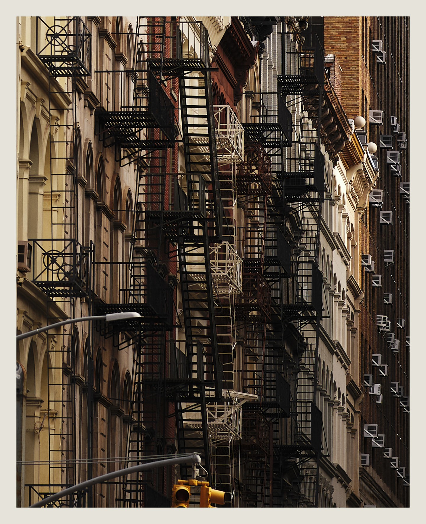 Urban architecture featuring rows of buildings with fire escapes, captured in daytime. The cityscape emphasizes depth and architectural details.