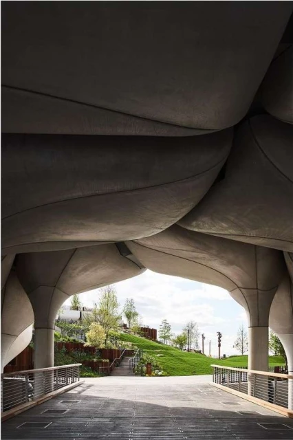 Architectural view of Little Island park in New York City with a green grassy landscape and grey concrete support structures.