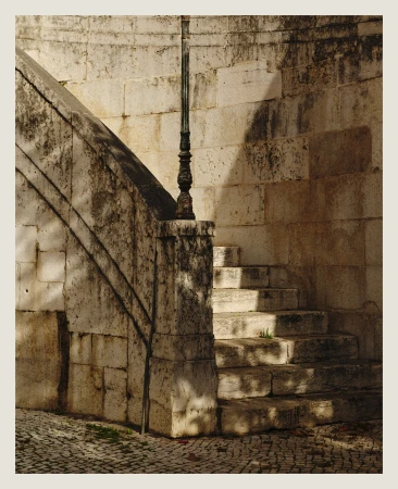 Stone staircase with ornate metal lamppost and shadows casting on the stairs and wall, creating a vintage architectural scene.
