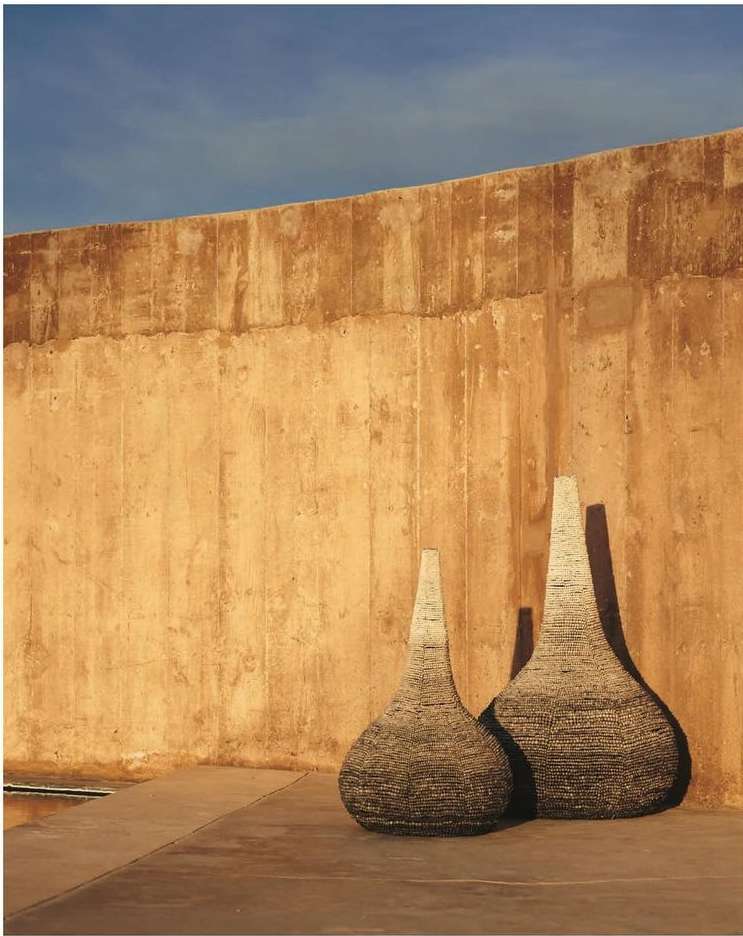 Two textured vases stand outdoors against a tall tan wall beneath a blue sky, exhibiting shades of brown, tan, and blue.