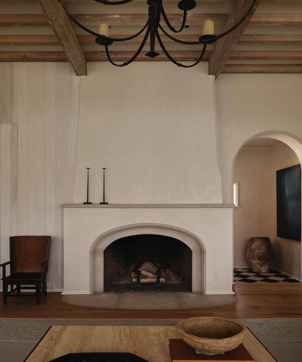 Interior view of a living room featuring a fireplace, arched doorway, wooden ceiling beams, and neutral color palette, exuding an inviting atmosphere.