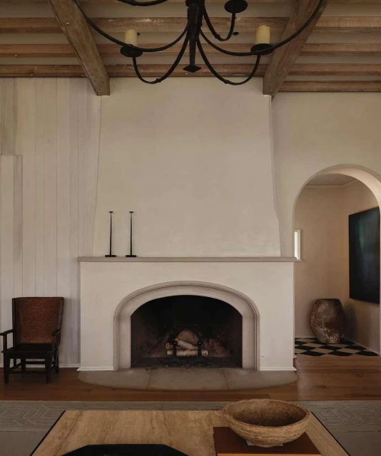 Interior view of a living room featuring a fireplace, arched doorway, wooden ceiling beams, and neutral color palette, exuding an inviting atmosphere.
