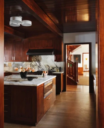 Interior view of a kitchen with wood cabinets, marble countertops, an island with a microwave, and an open doorway to a hallway.