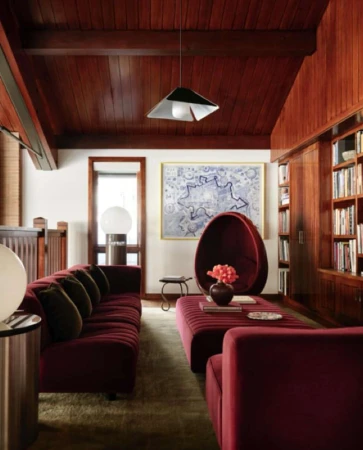 Interior view of a living room with a burgundy sofa and egg chair, complemented by wood paneling, a modern lamp, and a bookshelf.
