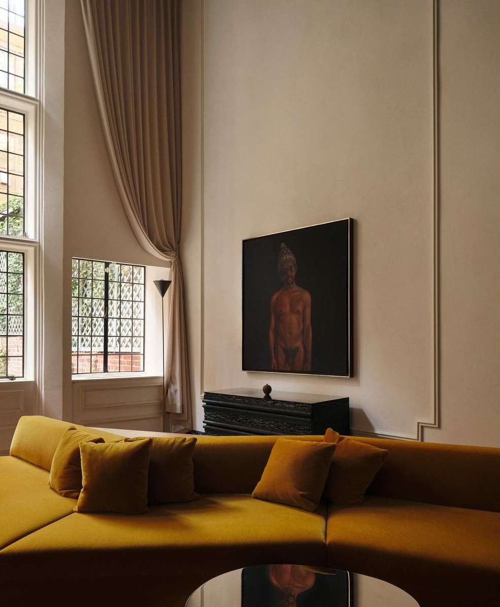 Living room interior featuring a mustard-yellow sectional sofa with pillows, a black accent table, and an art piece above it.