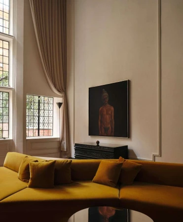 Living room interior featuring a mustard-yellow sectional sofa with pillows, a black accent table, and an art piece above it.
