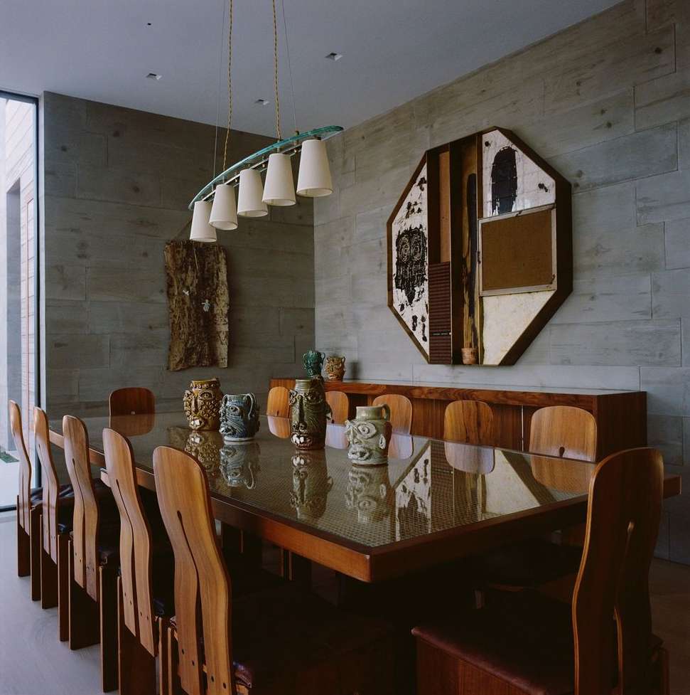 Modern dining room featuring a long wooden table and chairs, an overhead light fixture, a sideboard with decorative pots, and artwork.