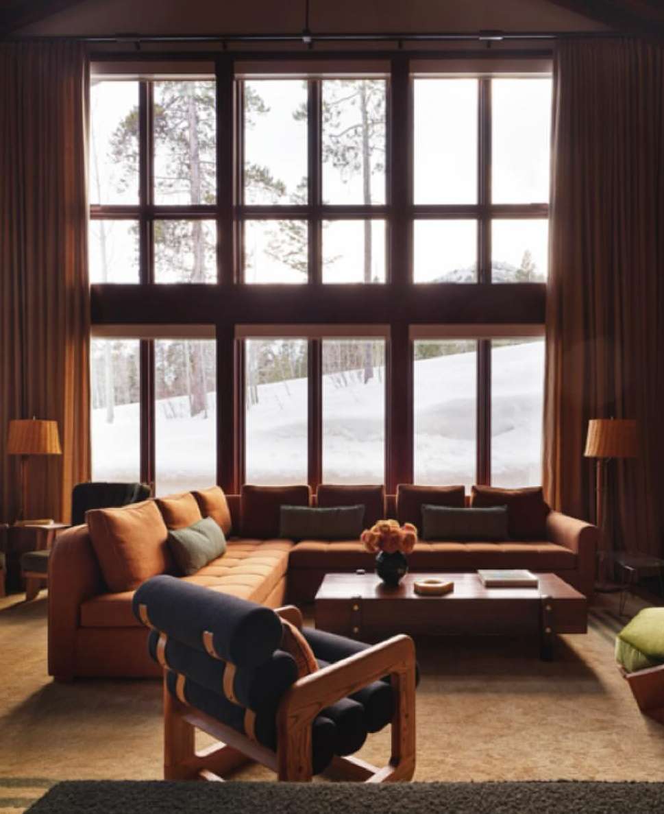 Living room interior with a large window overlooking a snowy landscape, featuring an L-shaped couch, accent chair, and natural light.
