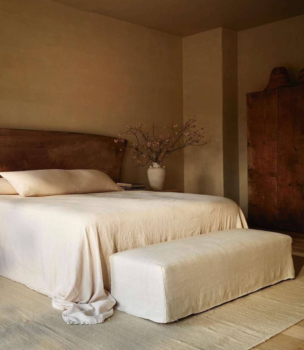 Bedroom interior featuring a neutral color palette with a wooden headboard, a bed with soft linens, and a wooden cabinet.