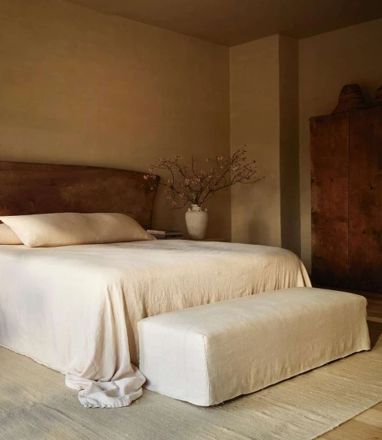 Bedroom interior featuring a neutral color palette with a wooden headboard, a bed with soft linens, and a wooden cabinet.