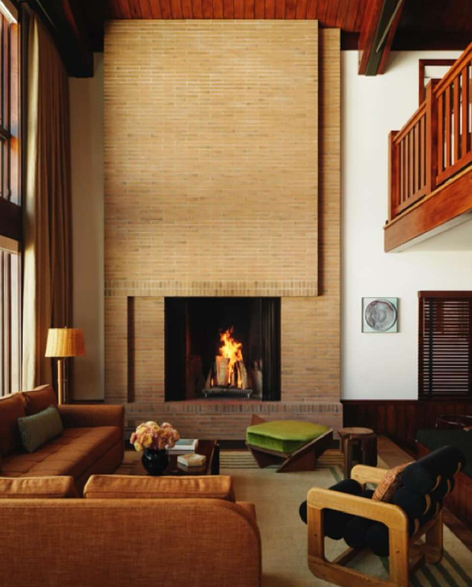 Living room interior featuring a brick fireplace, sofas, armchair, ottoman, rug, and wooden accents, creating a cozy and stylish atmosphere.