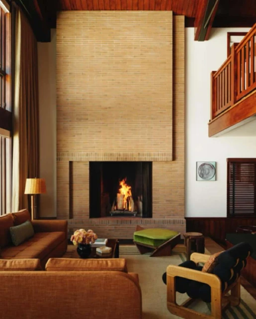 Living room interior featuring a brick fireplace, sofas, armchair, ottoman, rug, and wooden accents, creating a cozy and stylish atmosphere.