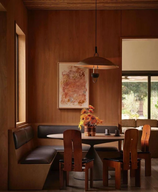Warm-toned interior dining space featuring wood paneling, an abstract painting, modern light fixture, and a dining table with unique chairs.