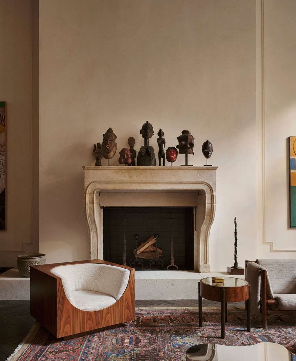 Living room features a fireplace with tribal sculptures, alongside a wooden chair and side table, complemented by a patterned rug.