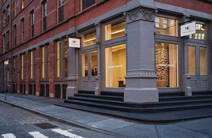 Exterior of Nordic Knots store in a red brick building with gray trim on a city street with a sign hanging by the entrance.