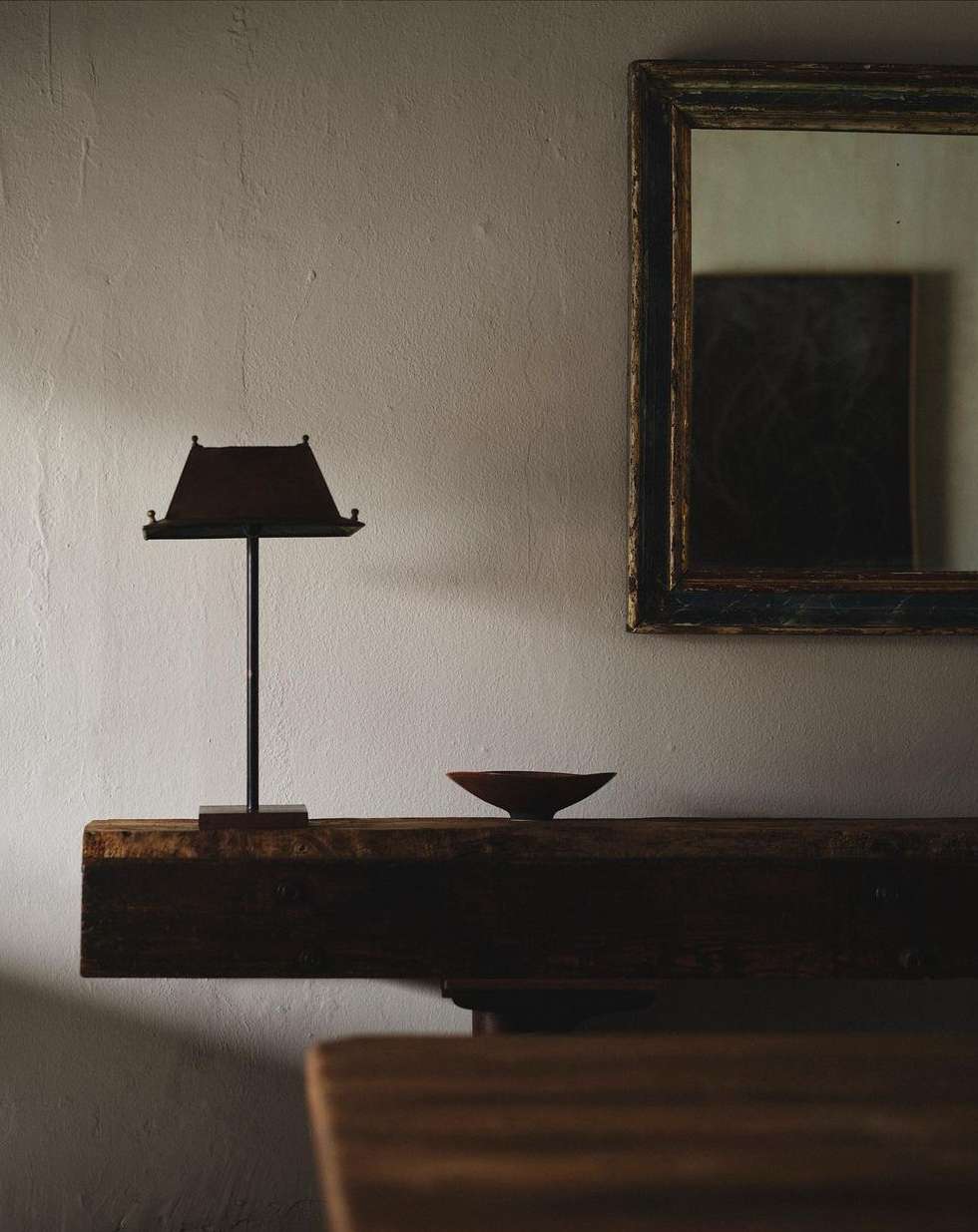 Interior scene with a small table lamp with a brown shade, a small dish, a rustic wooden shelf, and a framed picture on the wall.