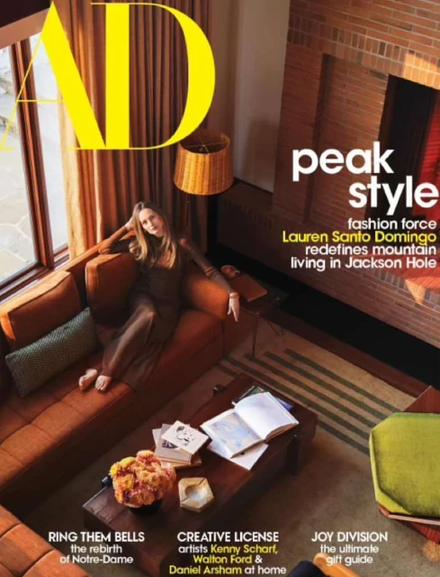 Magazine cover of Architectural Digest featuring woman on an orange couch, a coffee table with books, and interior design elements.