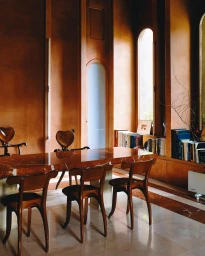 Interior shot of a dining room with a polished marble table, wooden chairs with heart-shaped backs, and warm terracotta-toned walls.