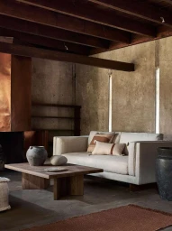 Interior shot of a minimalist living room featuring a beige sofa, wooden coffee table, and exposed ceiling beams photographed by Adrian Gaut.