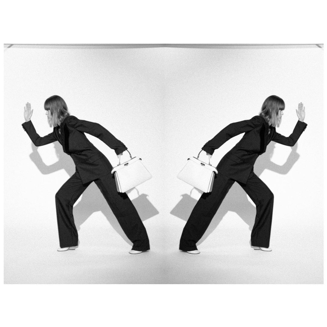 Monochrome fashion portrait of a model in a dark pantsuit holding a light handbag, photographed in London by Adrian Samson.