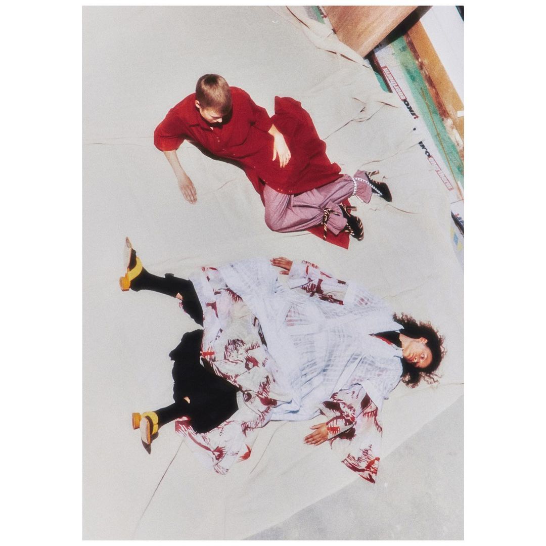 High-angle shot of two women lying on a light background wearing red and white patterned clothing and yellow heels.