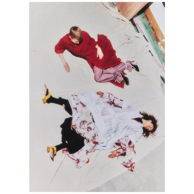 High-angle shot of two women lying on a light background wearing red and white patterned clothing and yellow heels.