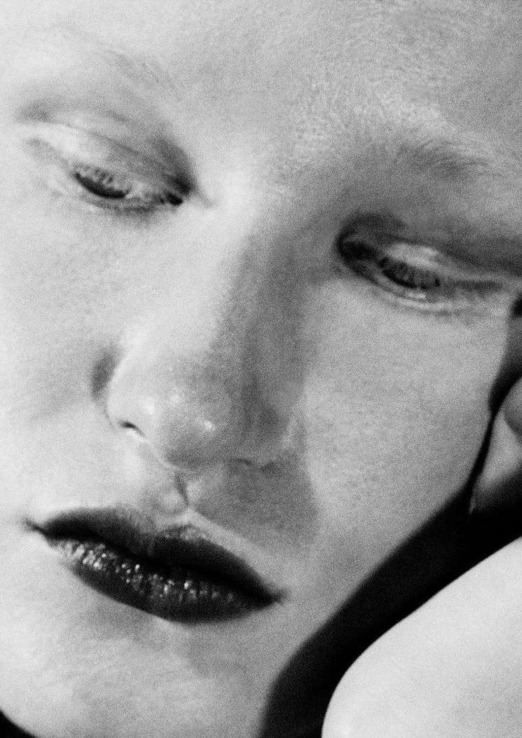Close-up black and white portrait of a young adult female with fair skin, dark lips, and closed eyes, creating a serene and intimate mood.