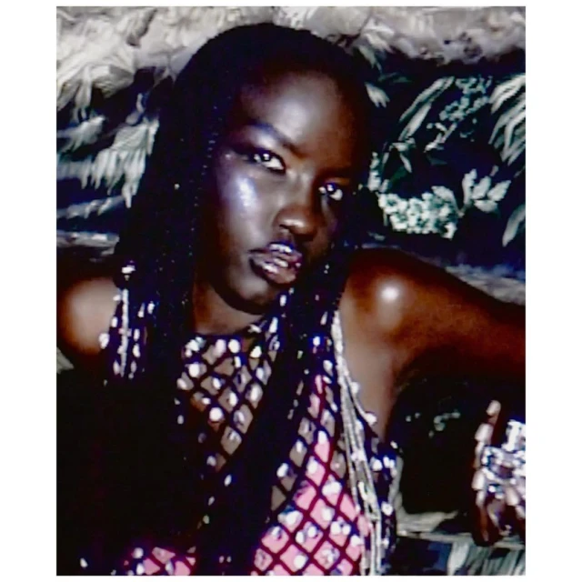 Fashion portrait of an African woman wearing a mesh top and heavy silver rings against a backdrop of leafy foliage.