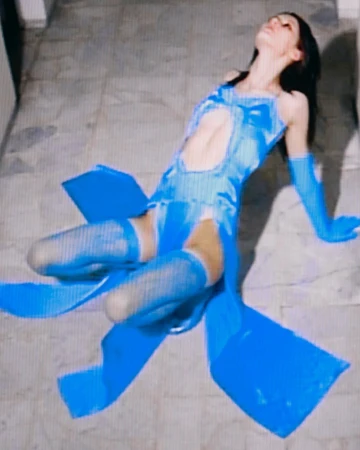 Woman in vibrant blue cutout dress and matching gloves lying on a stone surface